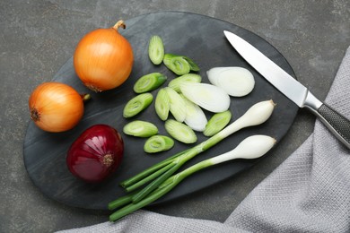 Board with different kinds of onions and knife grey table, flat lay