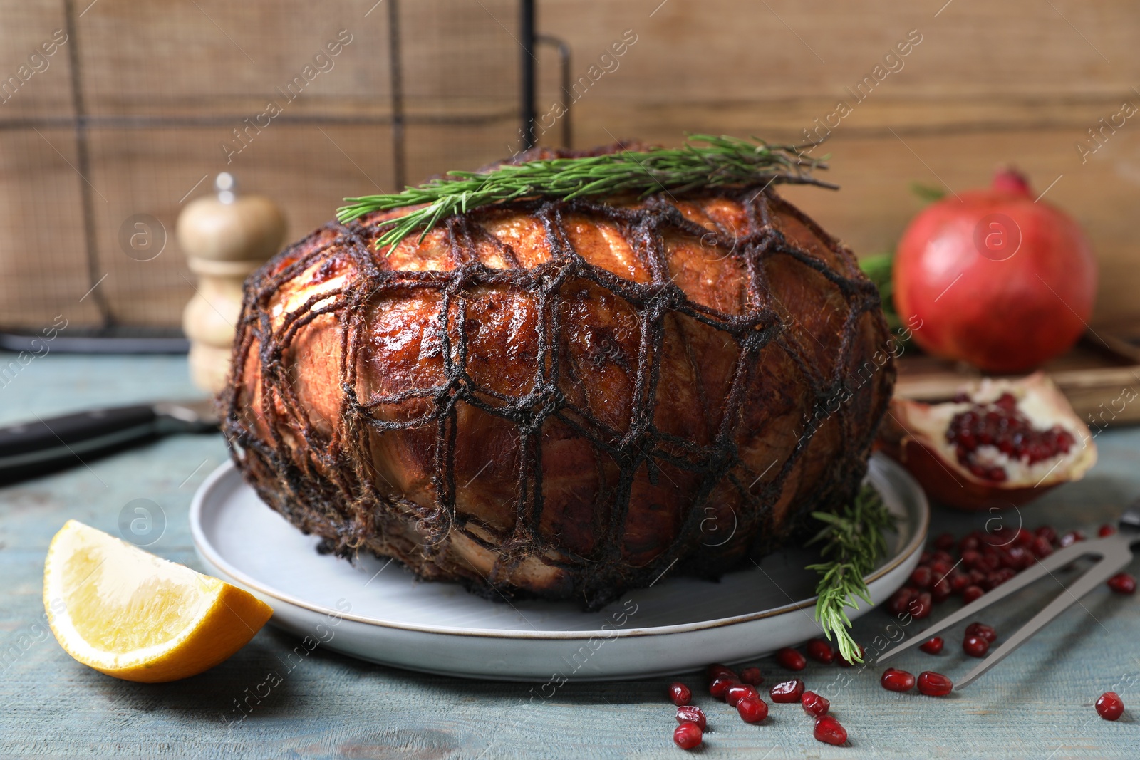 Photo of Delicious baked ham, carving fork, orange slice, pomegranate seeds and rosemary on rustic wooden table