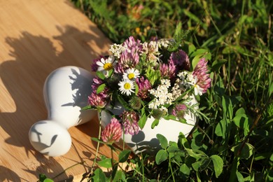 Photo of Ceramic mortar with pestle, different wildflowers and herbs on green grass outdoors