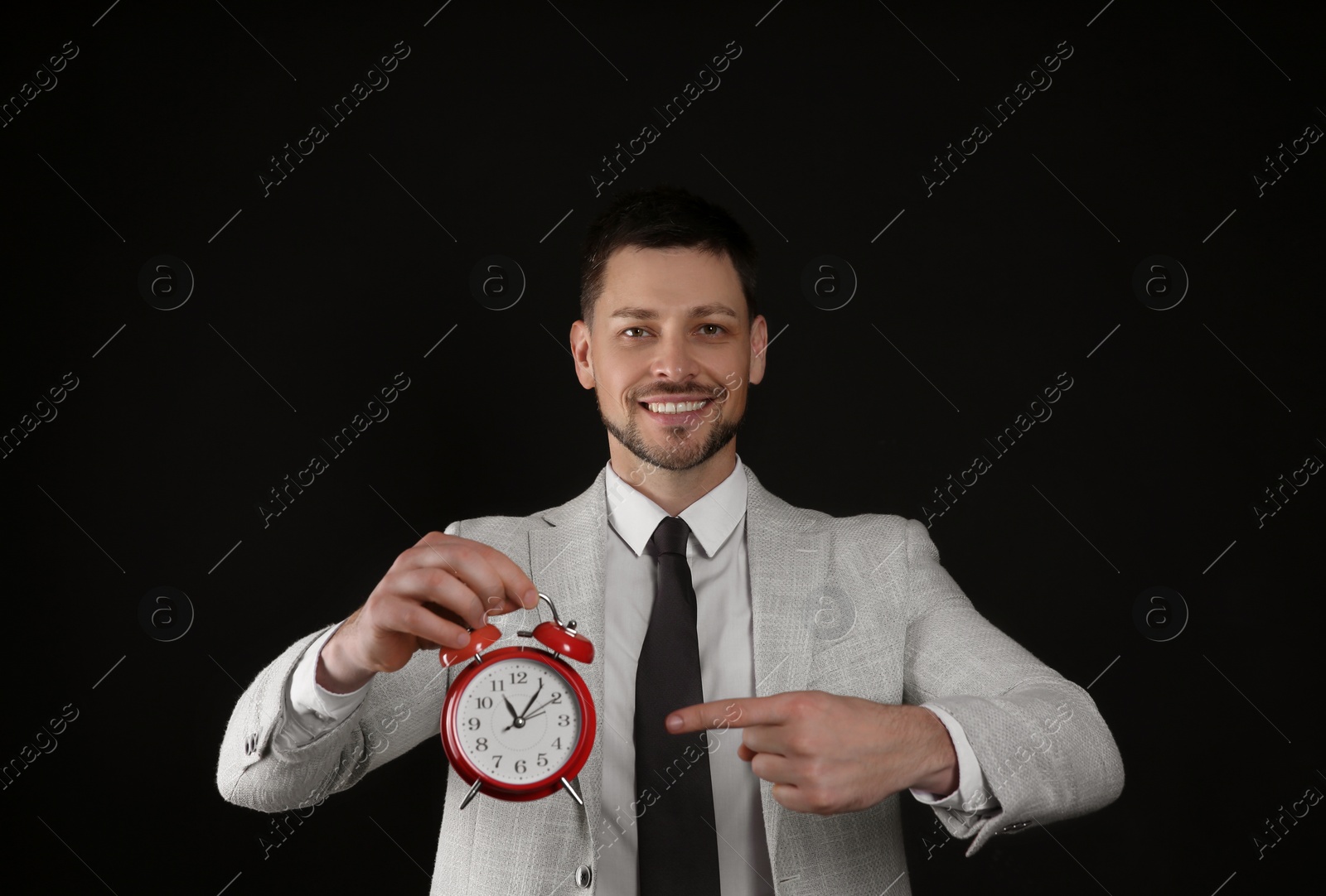 Photo of Happy businessman pointing on alarm clock against black background. Time management