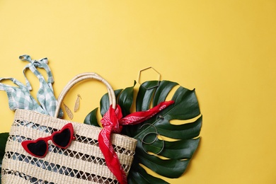 Stylish straw bag and summer accessories on yellow background, flat lay. Space for text