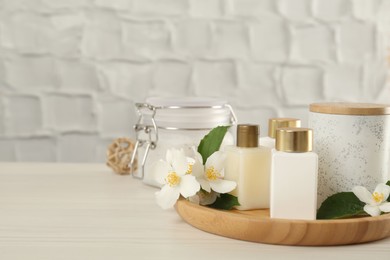 Photo of Beautiful jasmine flowers and skin care products on white wooden table, space for text