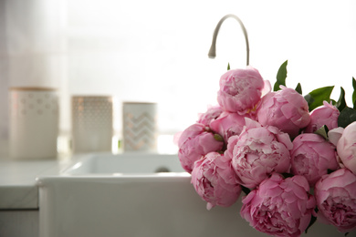 Photo of Bouquet of beautiful pink peonies in kitchen sink. Space for text