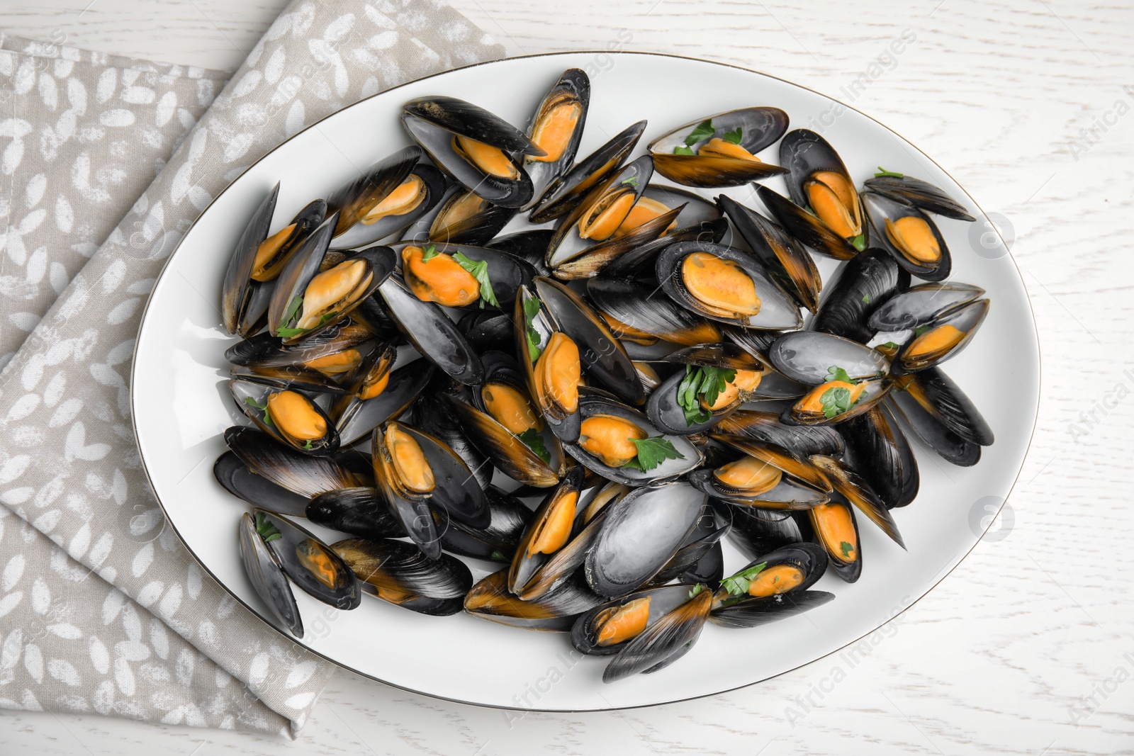 Photo of Plate of cooked mussels with parsley on white wooden table, top view