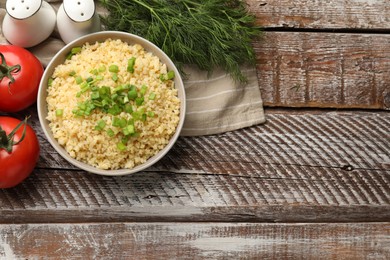 Delicious bulgur with green onion in bowl, tomatoes and dill on wooden table, top view. Space for text