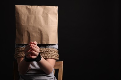 Photo of Little boy in paper bag tied up and taken hostage on dark background. Space for text