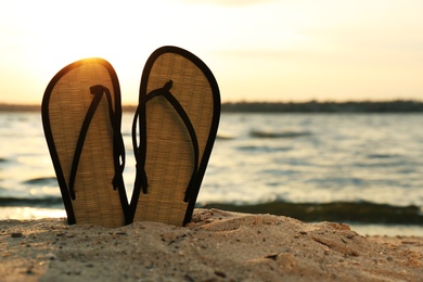 Stylish flip flops on sand near sea, space for text. Beach accessories