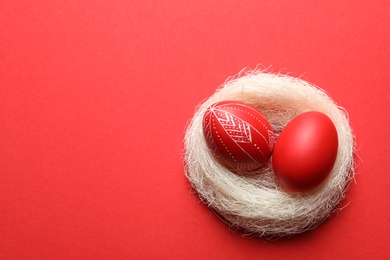 Photo of Nest with red painted Easter eggs on table, above view. Space for text