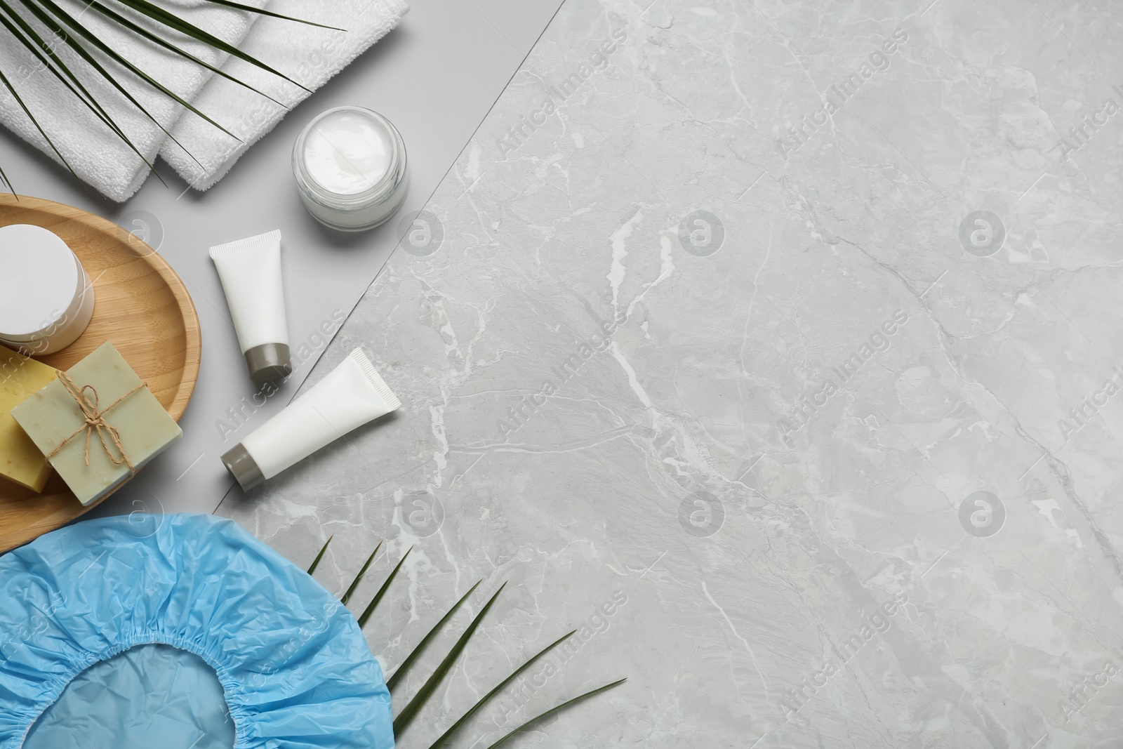 Photo of Flat lay composition with shower cap and toiletries on grey marble background. Space for text