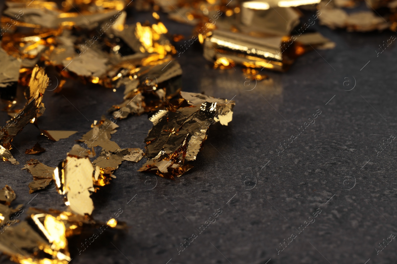 Photo of Pieces of edible gold leaf on textured table, closeup. Space for text