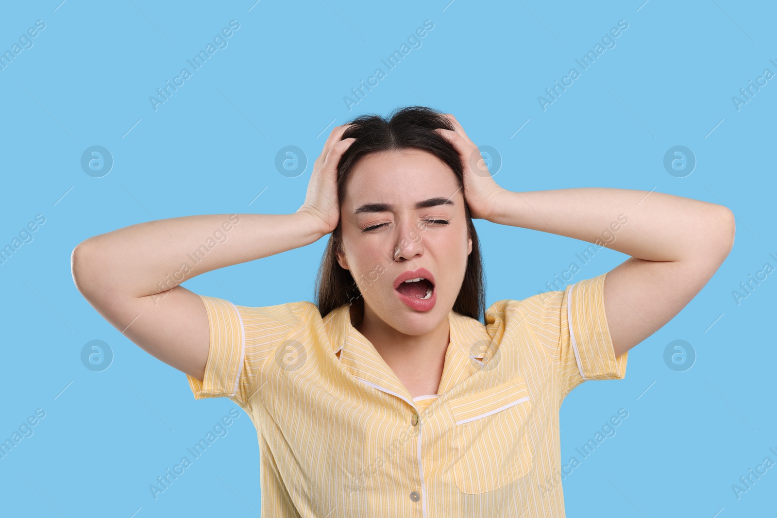 Photo of Tired young woman yawning on light blue background. Insomnia problem