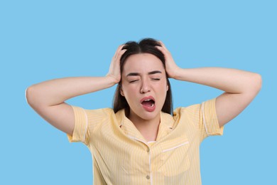 Photo of Tired young woman yawning on light blue background. Insomnia problem