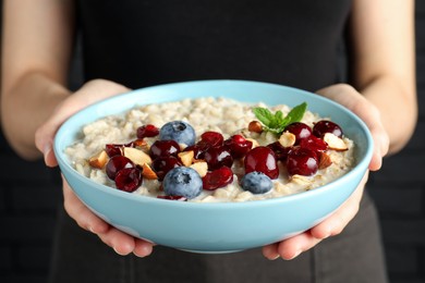 Woman holding bowl of oatmeal porridge with berries on black background, closeup