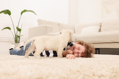 Photo of Little boy with cute puppy on beige carpet indoors