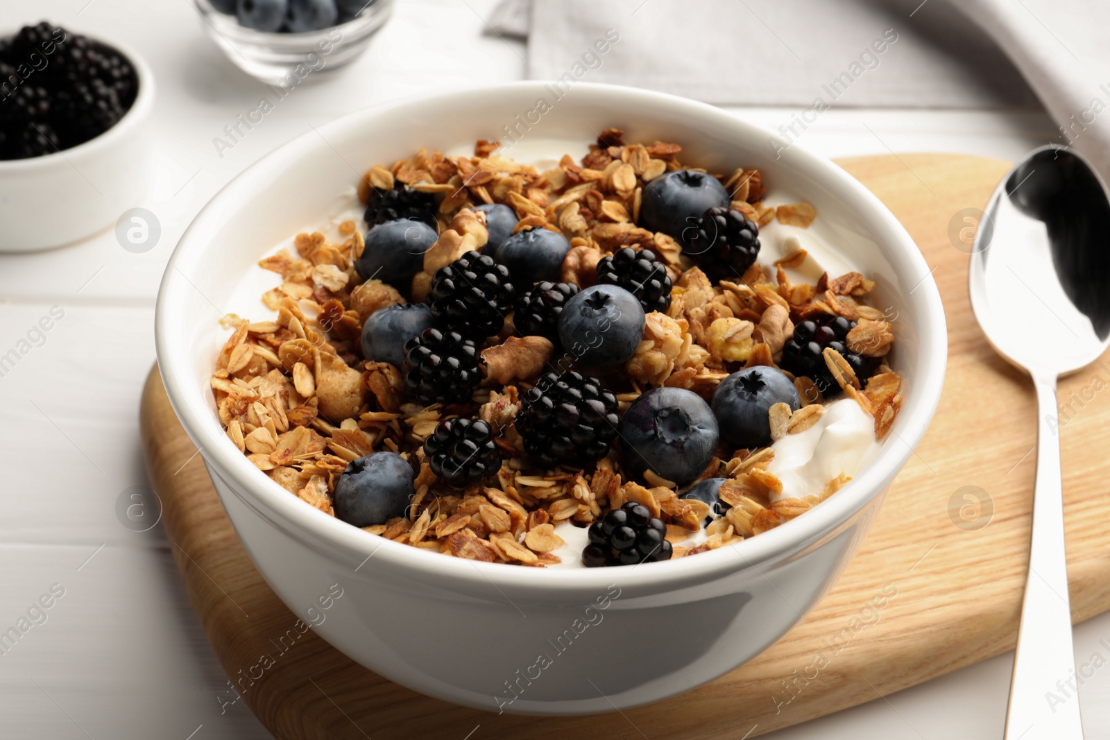 Photo of Bowl of healthy muesli served with berries on white wooden table, closeup