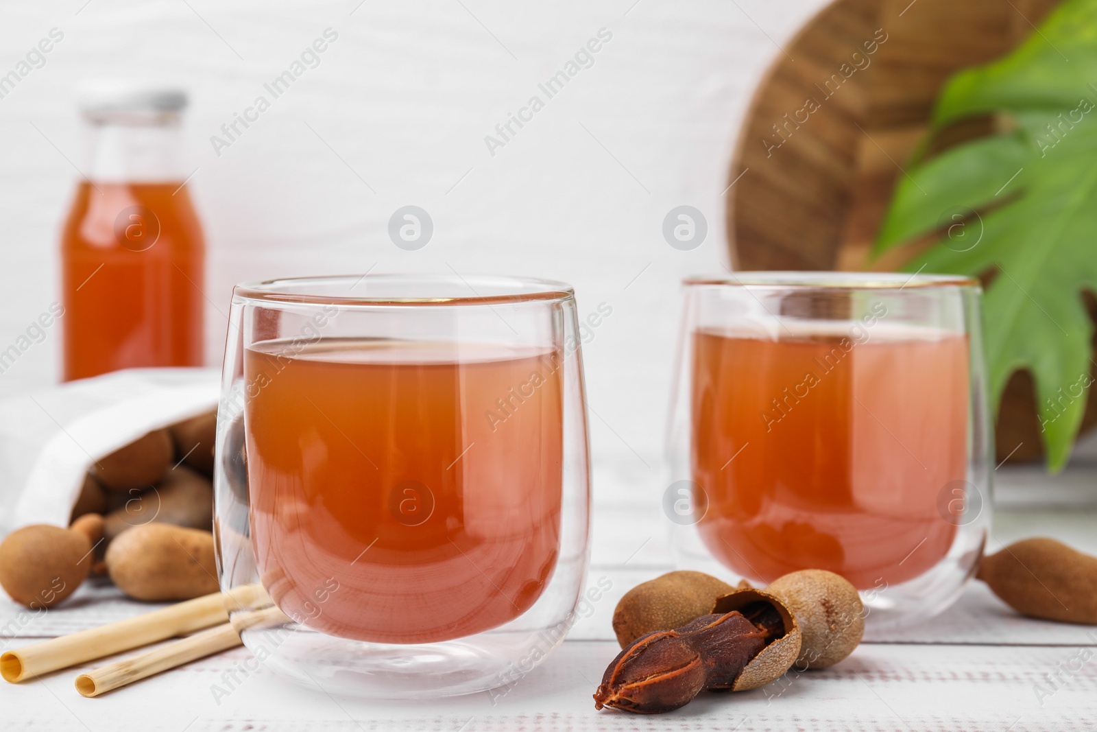 Photo of Tamarind juice and fresh fruits on white wooden table, closeup