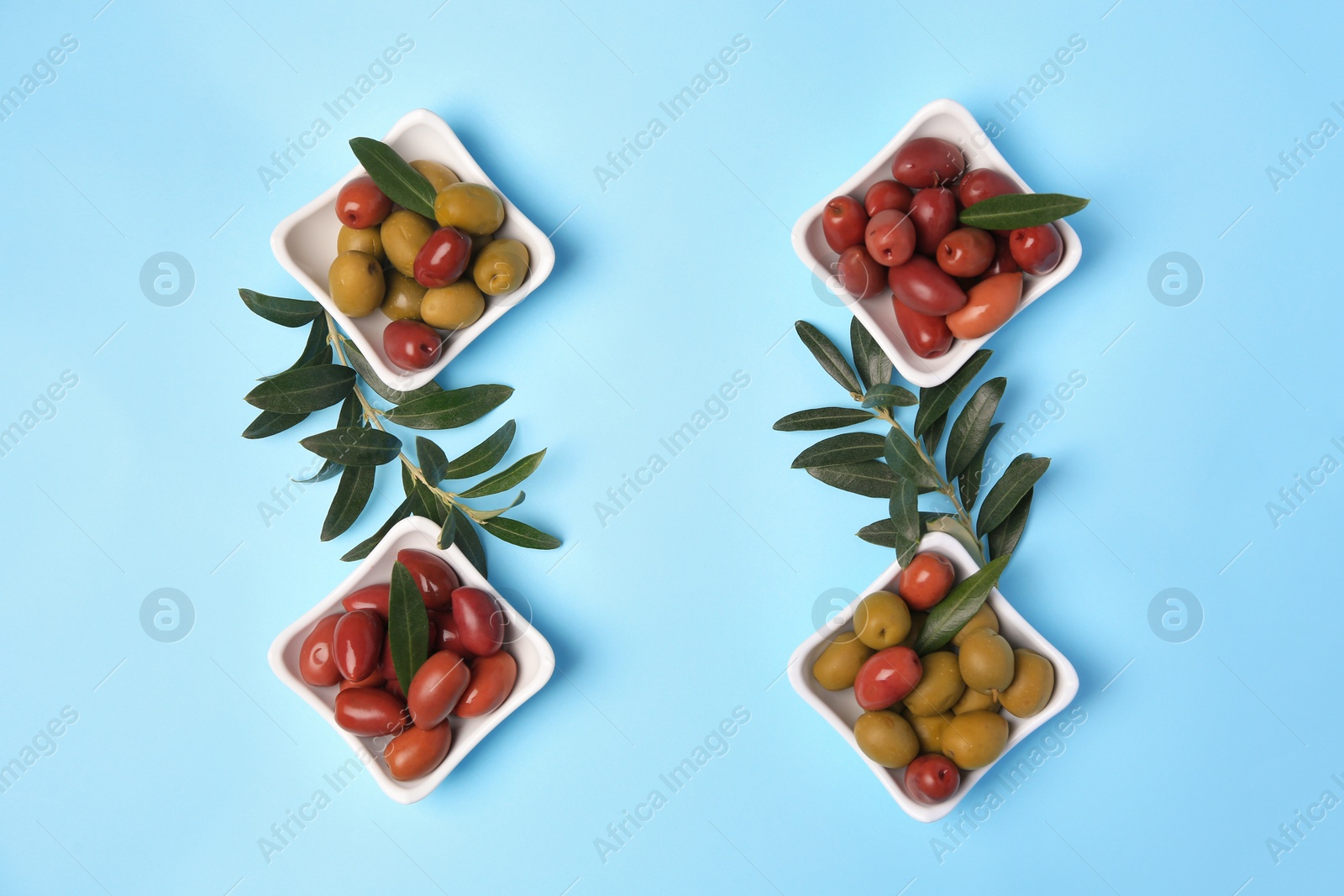 Photo of Different fresh olives and green leaves on light blue background, flat lay