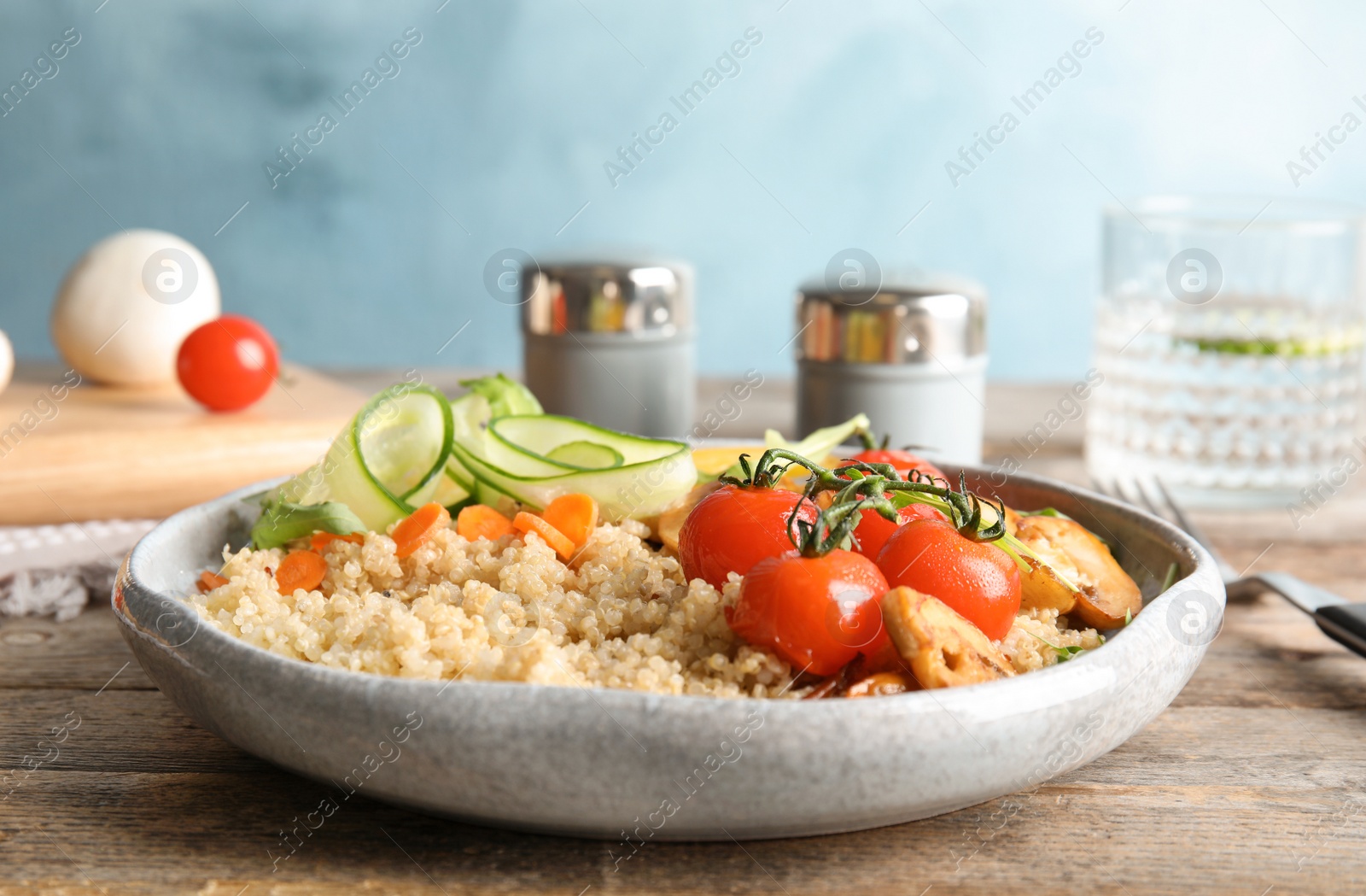 Photo of Plate with healthy quinoa salad and vegetables served on wooden table