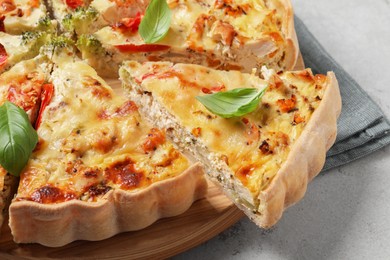 Tasty quiche with chicken, vegetables, basil and cheese on light textured table, closeup