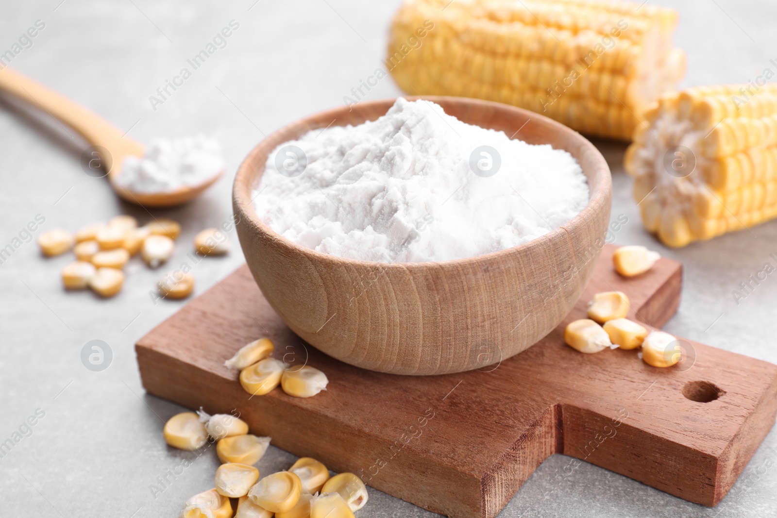 Photo of Bowl with corn starch and kernels on light grey table, closeup