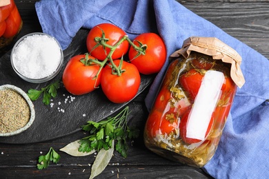 Flat lay composition with pickled tomatoes in glass jar on black wooden table