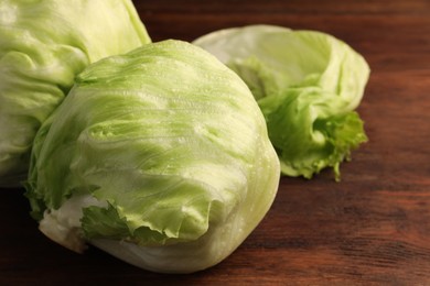 Photo of Fresh green iceberg lettuce heads and leaves on wooden table, closeup