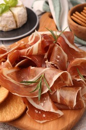 Slices of tasty cured ham, crackers and rosemary on wooden board, closeup