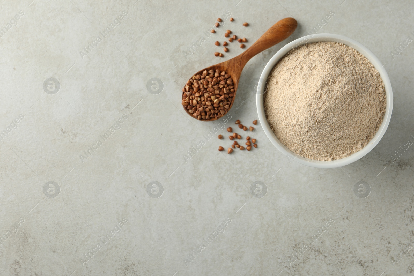Photo of Bowl of flour and spoon with buckwheat on light grey table, flat lay. Space for text