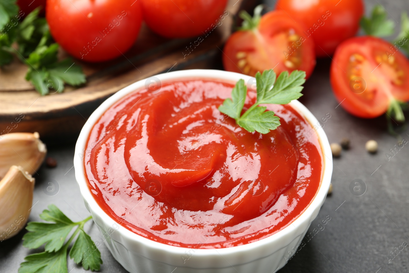 Photo of Delicious tomato ketchup in bowl, parsley and garlic on grey table, closeup