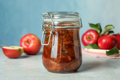 Photo of Tasty apple jam in glass jar and fresh fruits on light table