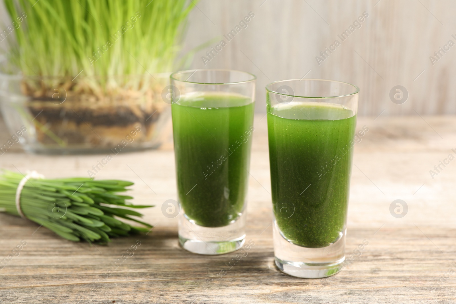 Photo of Wheat grass drink in shot glasses on wooden table, closeup