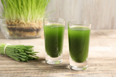 Photo of Wheat grass drink in shot glasses on wooden table, closeup