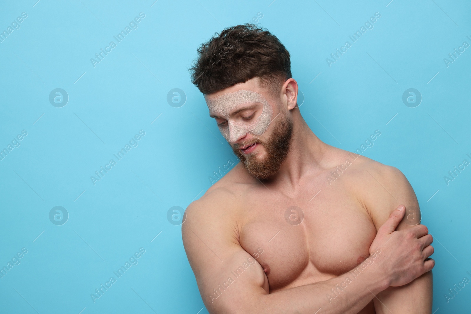 Photo of Handsome man with facial mask on his face against light blue background, space for text