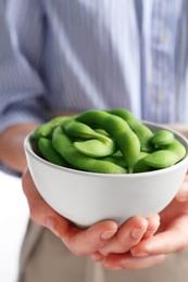 Woman holding bowl with green edamame beans in pods on white background, closeup
