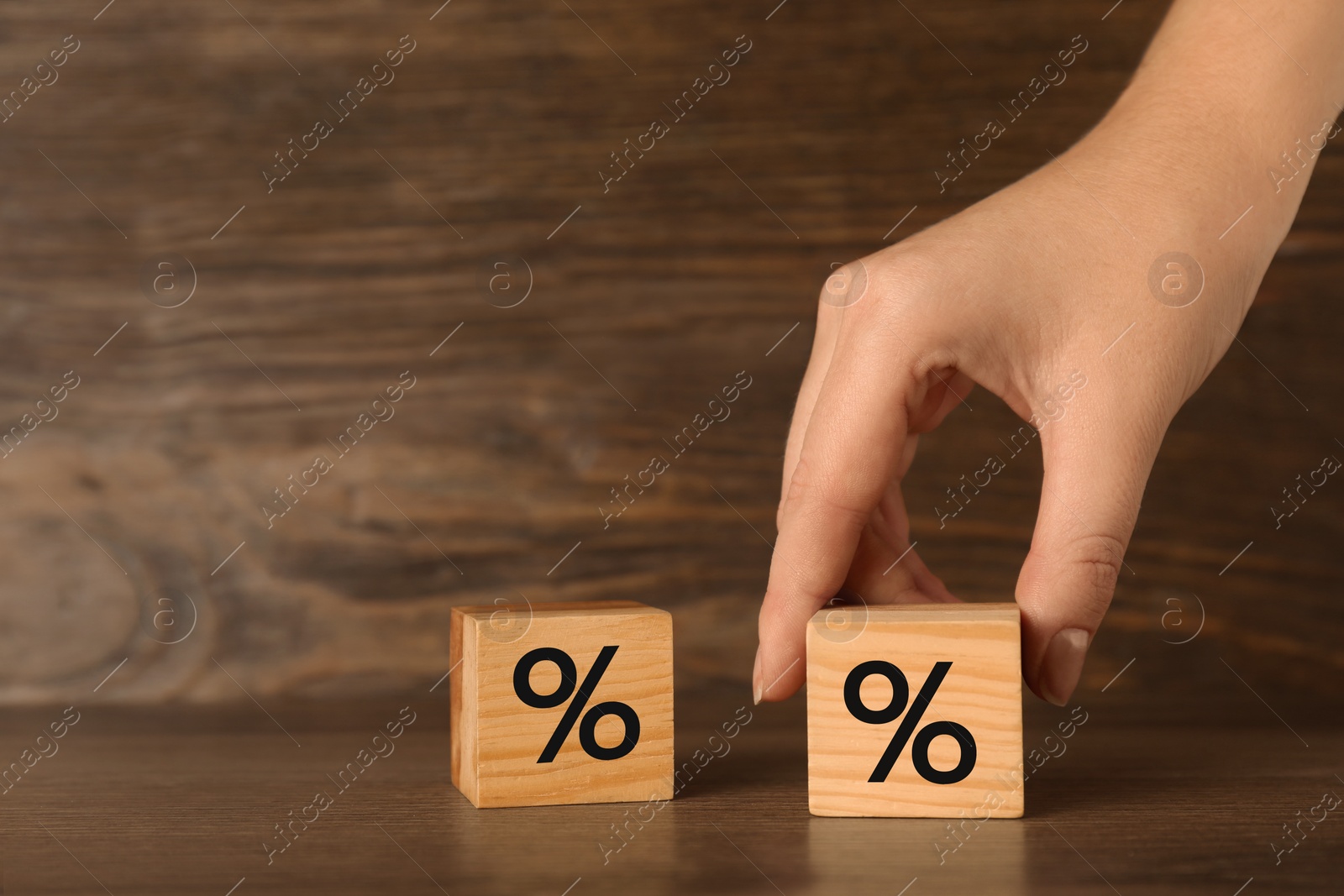 Photo of Woman holding wooden cube with percent sign at table, closeup. Space for text