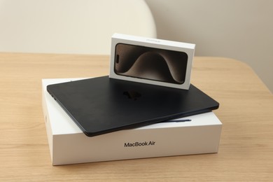 Photo of Leiden, Netherlands - October 6, 2023: Modern black MacBook Air and box from iPhone 15 Pro Max on wooden table