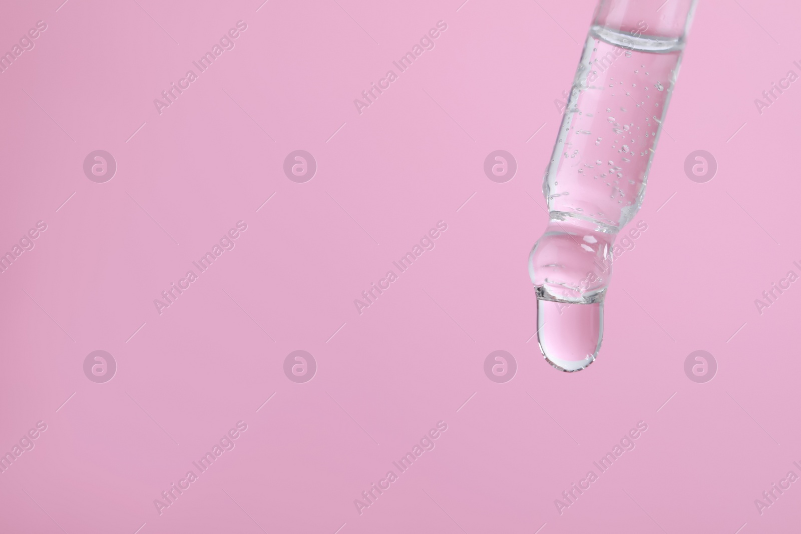 Photo of Dripping serum from pipette on pink background, closeup. Space for text