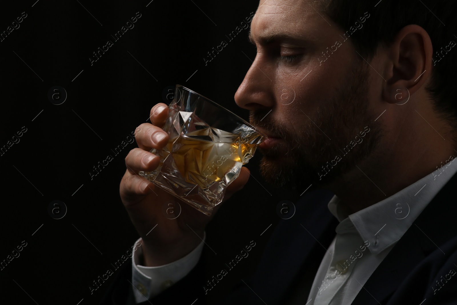 Photo of Man in suit drinking whiskey on black background