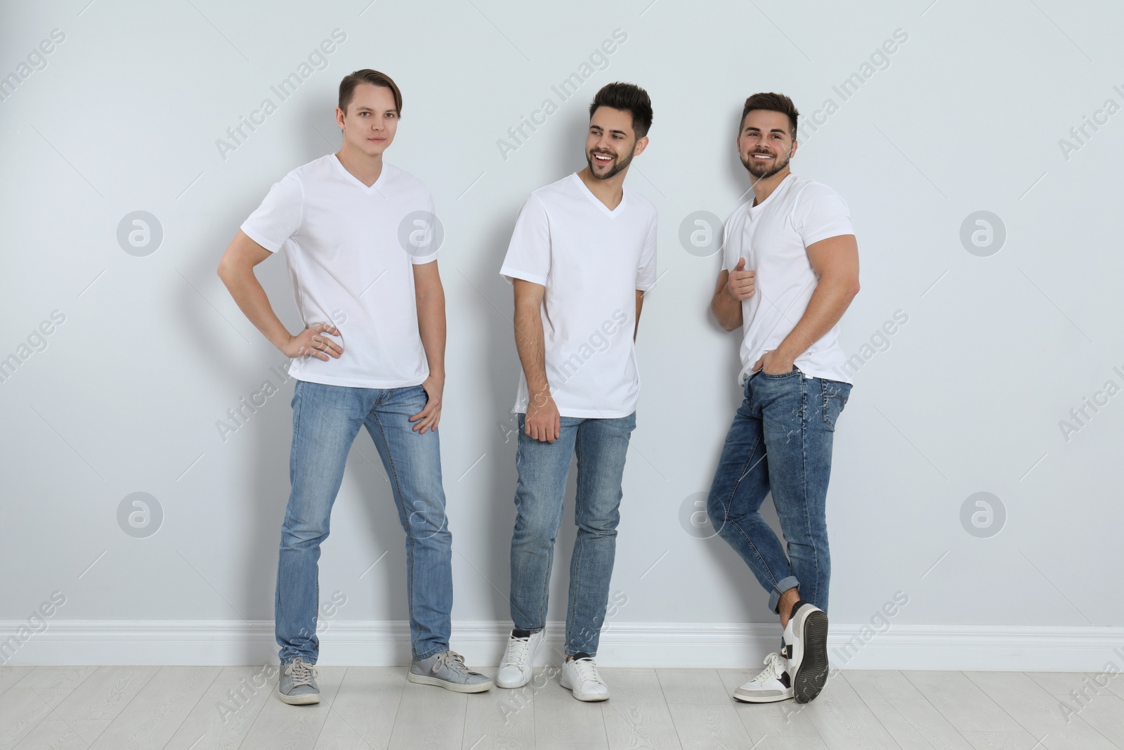 Photo of Group of young men in stylish jeans near light wall