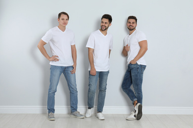 Group of young men in stylish jeans near light wall