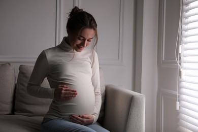 Photo of Young pregnant woman sitting on sofa at home