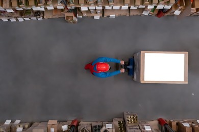 Man working with pallet truck at warehouse, top view. Logistics center