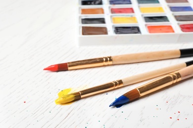 Brushes and plastic palette with colorful paints on light background