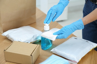 Woman applying antiseptic gel onto wipe while cleaning parcels at wooden table, closeup. Preventive measure during COVID-19 pandemic