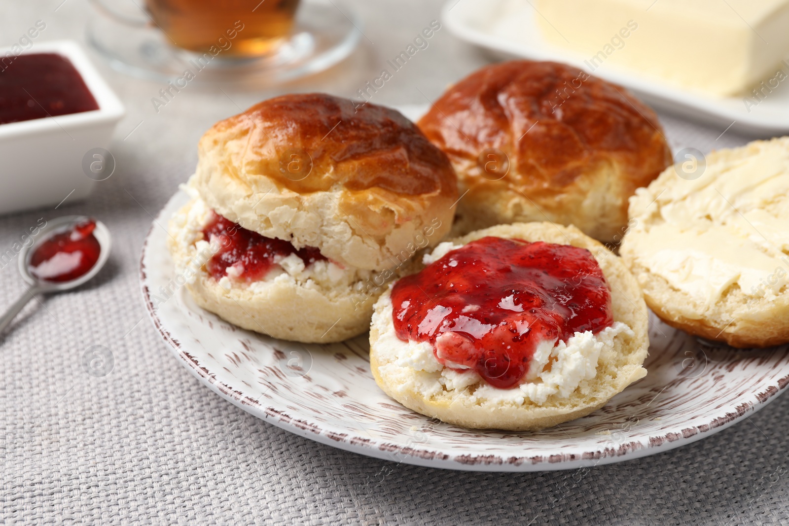 Photo of Freshly baked soda water scones with cranberry jam and butter on light grey mat, closeup