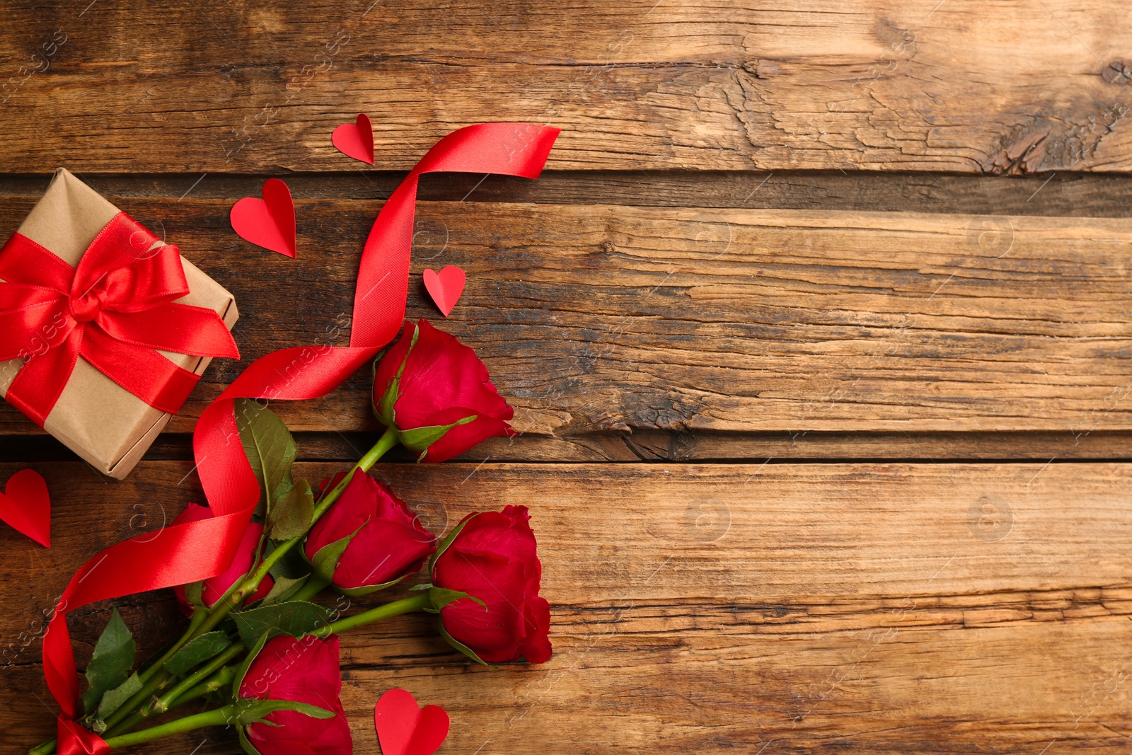 Photo of Flat lay composition with gift box and roses on wooden table. Valentine's Day celebration