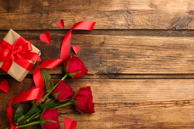 Photo of Flat lay composition with gift box and roses on wooden table. Valentine's Day celebration