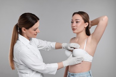 Mammologist checking woman's breast on gray background