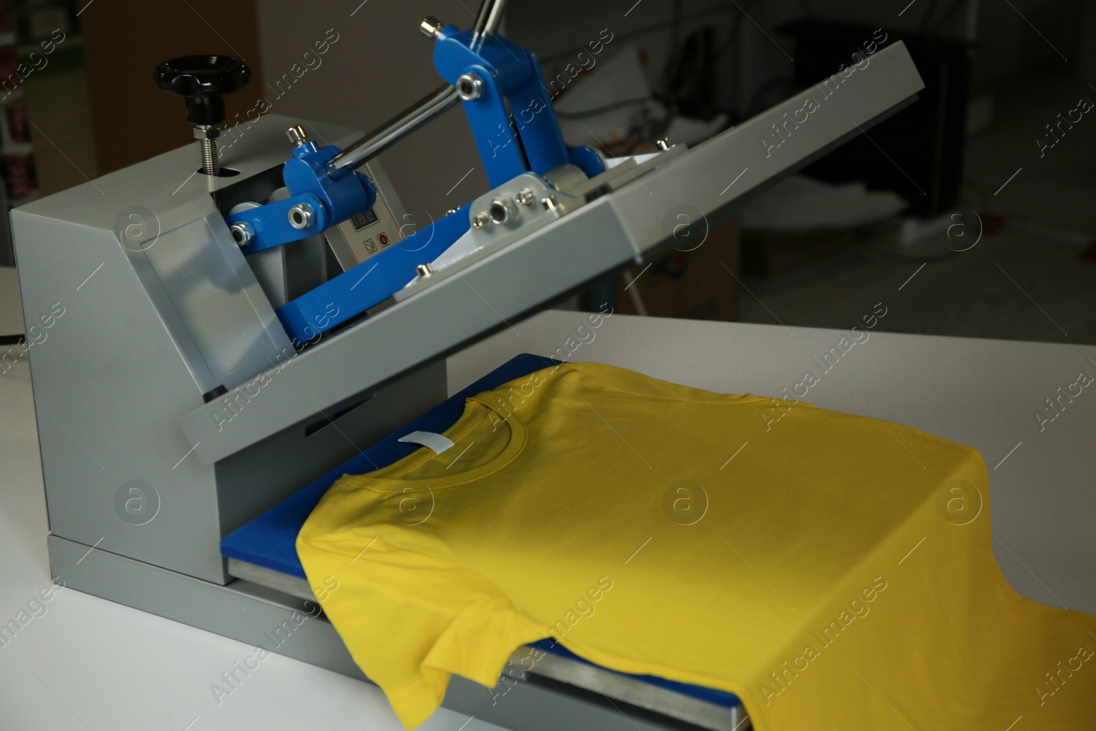 Photo of Printing logo. Heat press with yellow t-shirt on white table