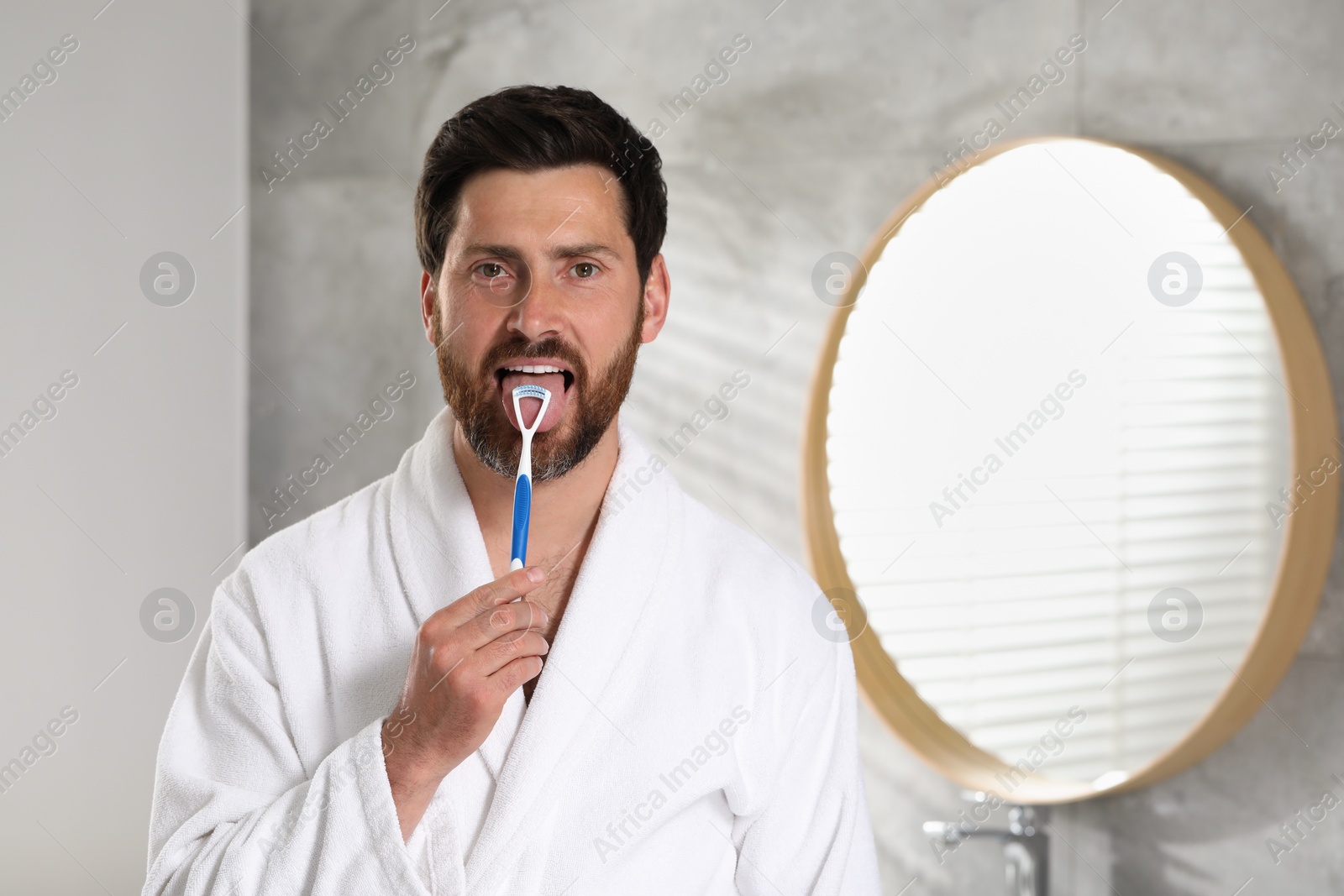 Photo of Handsome man brushing his tongue with cleaner in bathroom, space for text